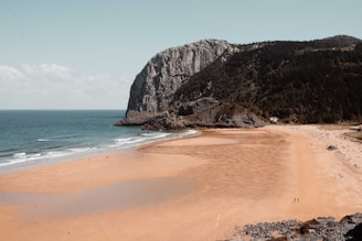 brown sand beach near brown rocky mountain under blue sky during daytime