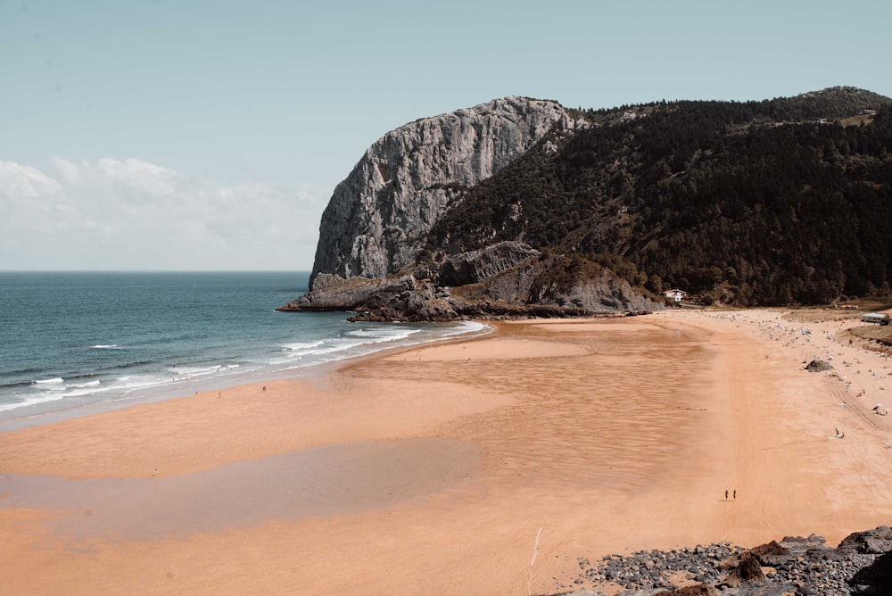 brown sand beach near brown rocky mountain under blue sky during daytime