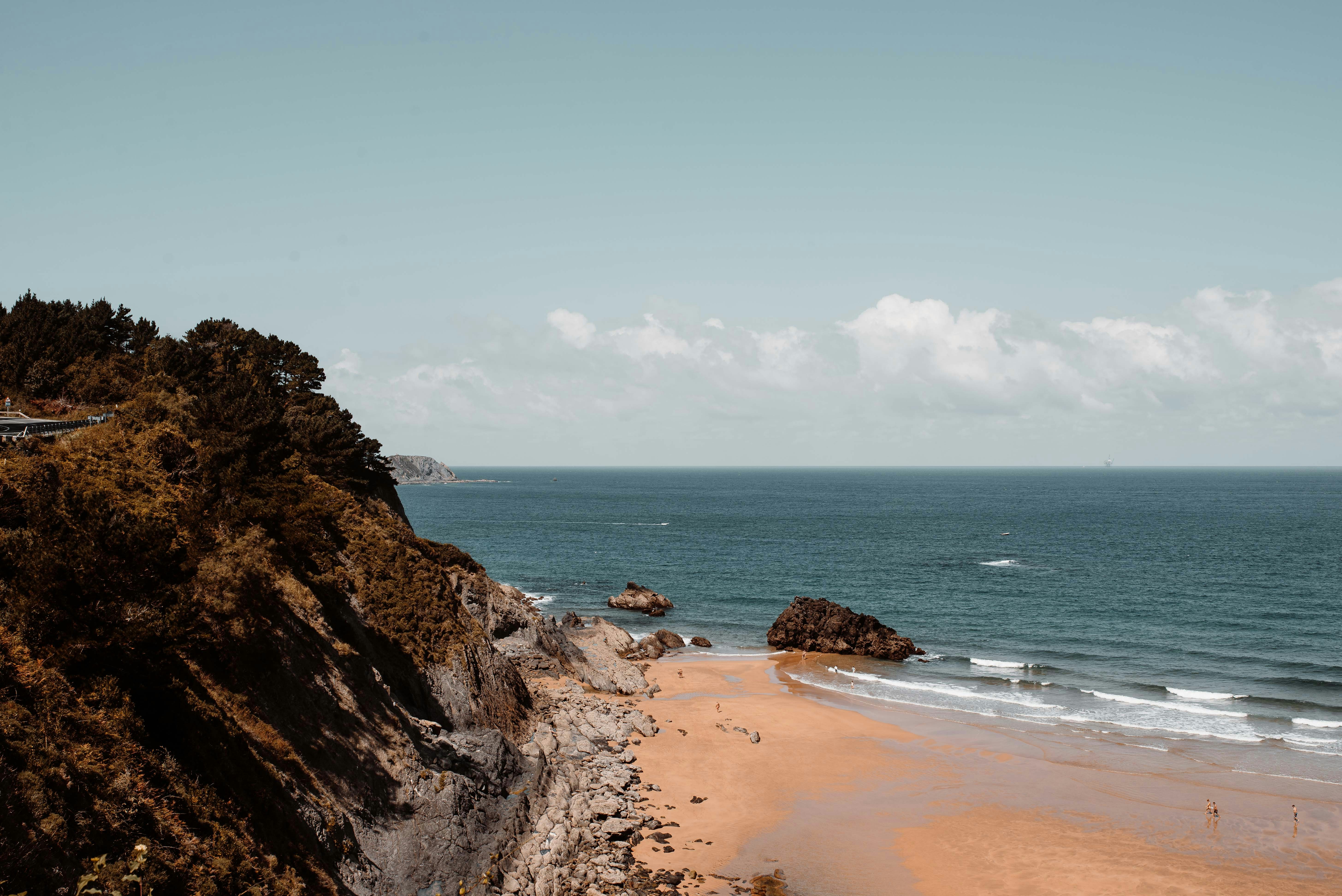 brown rocky mountain beside body of water during daytime, Stumbled upon this stunning beach, driving down the Basque Country coast. 