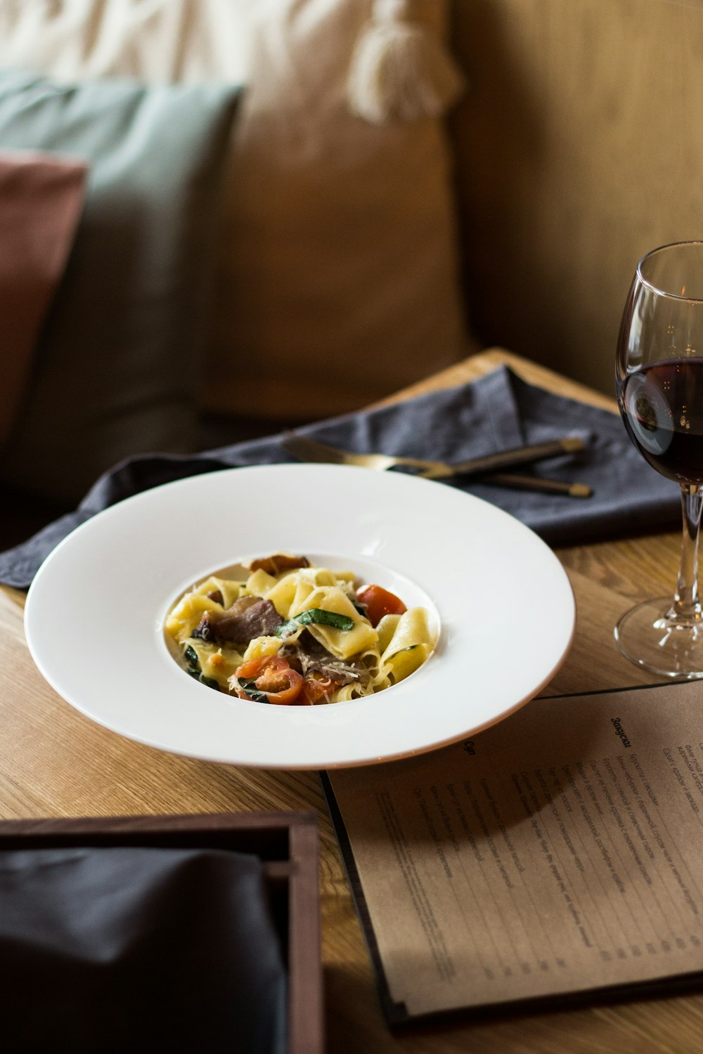 pasta dish on white ceramic plate beside wine glass