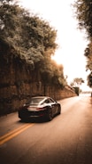Sleek black sports car speeding on an open highway at sunset.