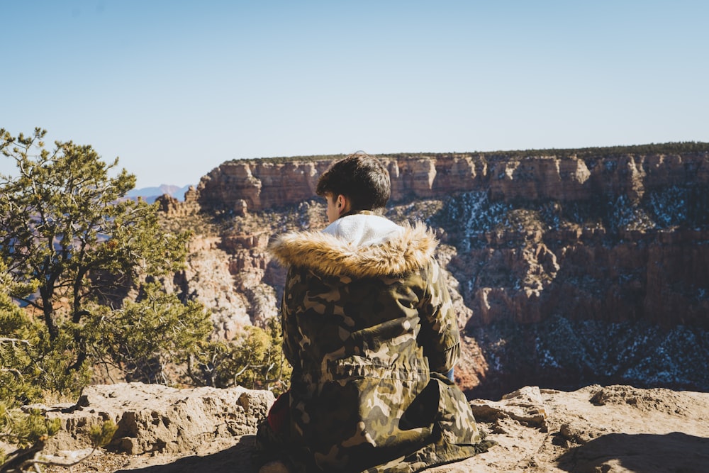 woman in brown fur coat sitting on rock formation during daytime