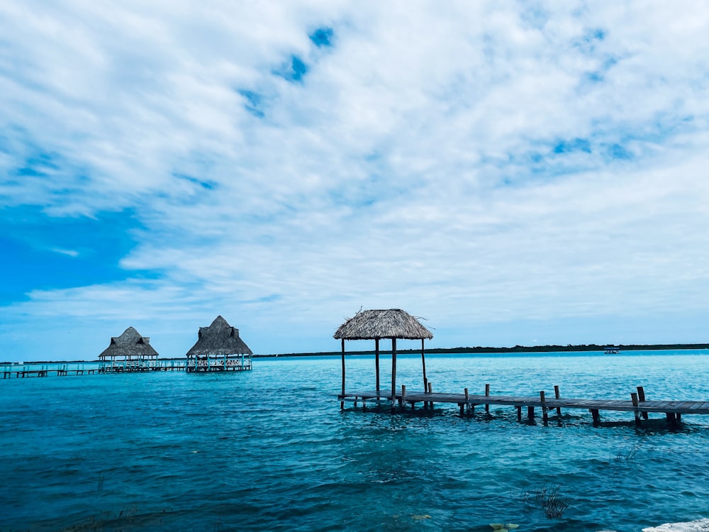 brown wooden beach house on blue sea under blue sky and white clouds during daytime