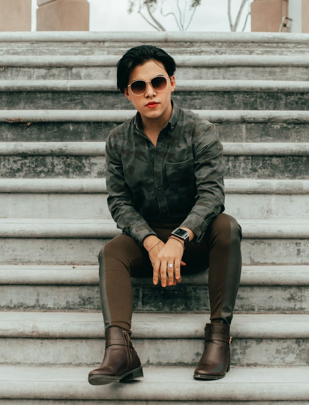 man in black leather jacket and brown pants wearing black sunglasses sitting on white concrete stairs