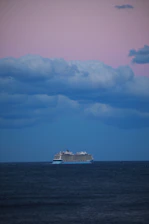 A serene cruise ship gliding through calm blue waters under a purple twilight sky.