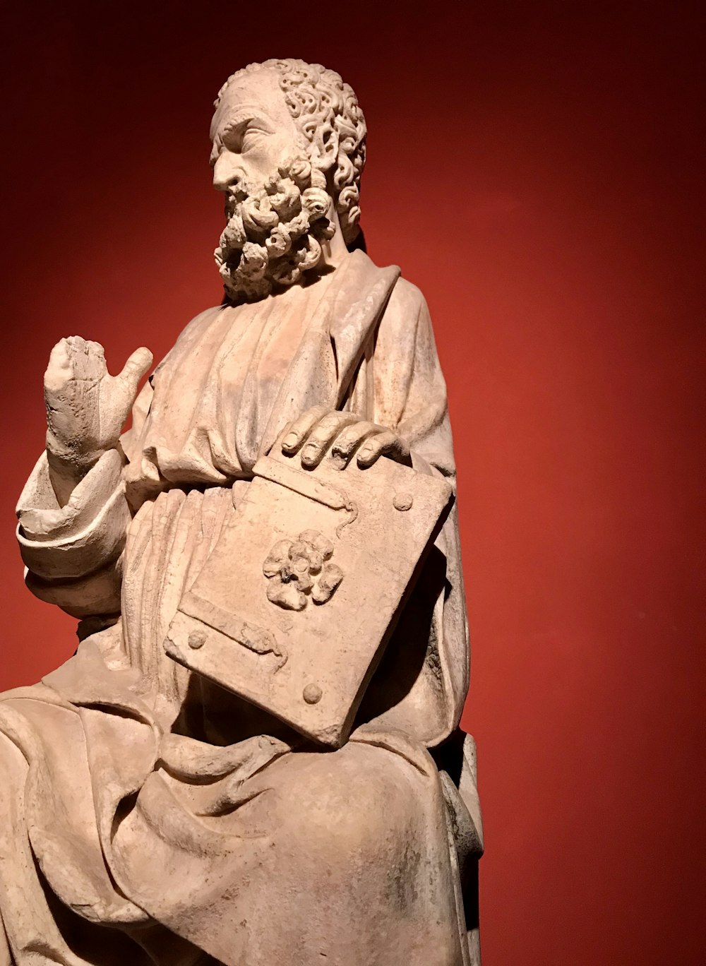 man in brown coat holding book statue