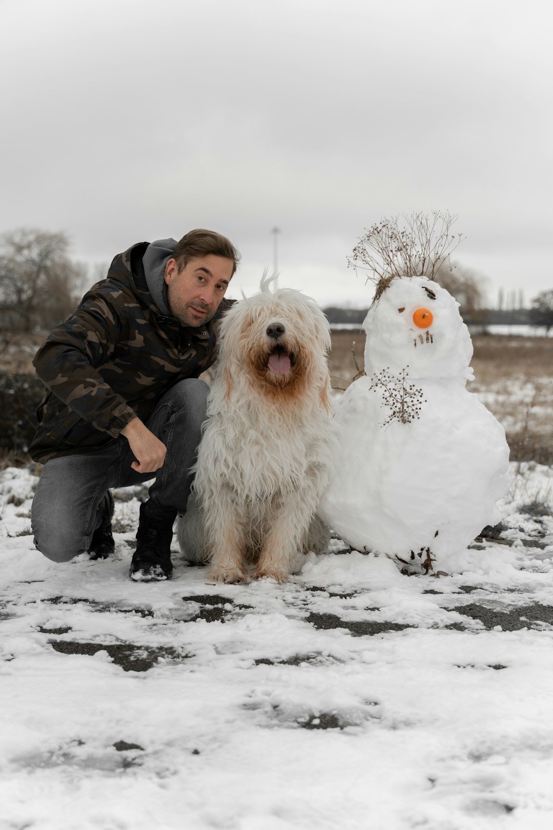 man in black jacket sitting on snow covered ground with white snowman during daytime