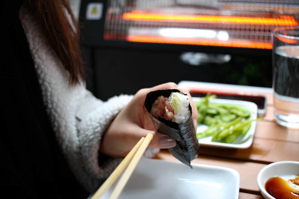 Persona sosteniendo un sushi en un plato de cerámica blanca