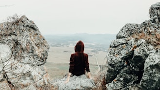 woman in brown hoodie sitting on rock formation during daytime