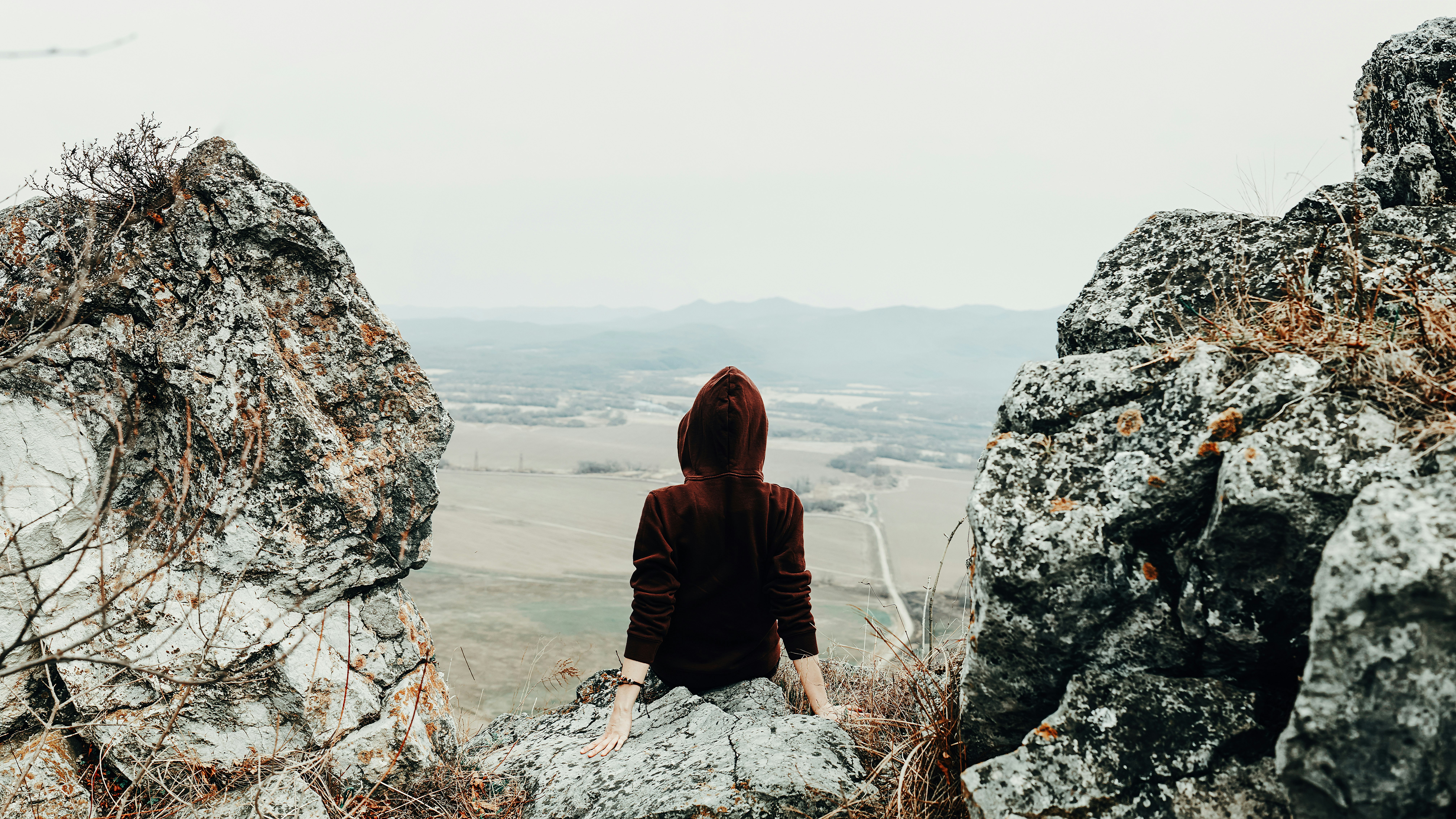 woman in brown hoodie sitting on rock formation during daytime