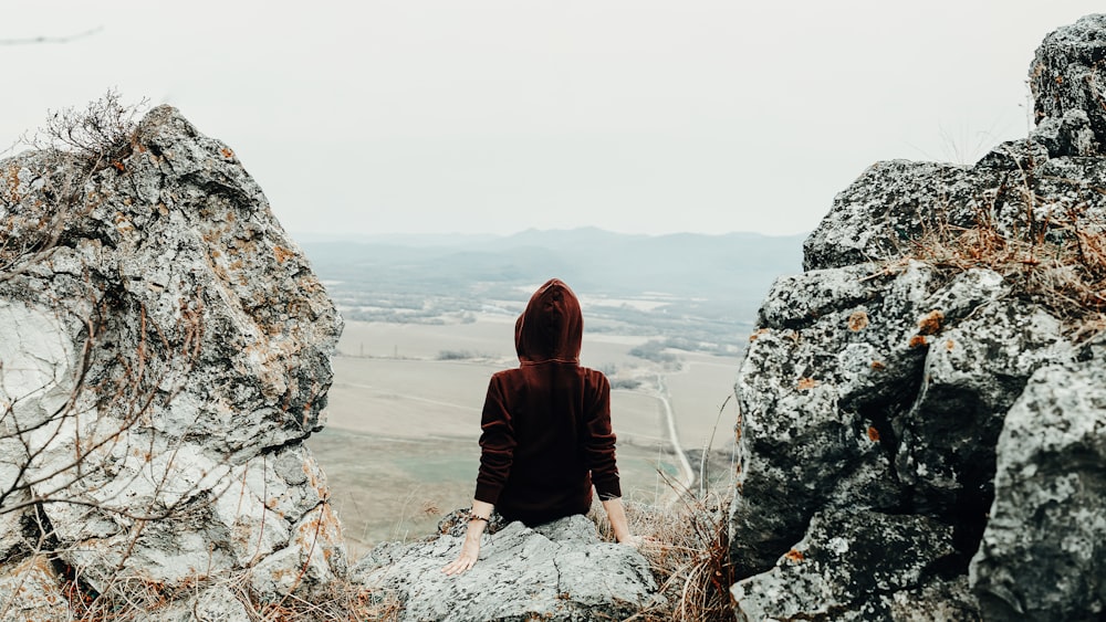 woman in brown hoodie sitting on rock formation during daytime