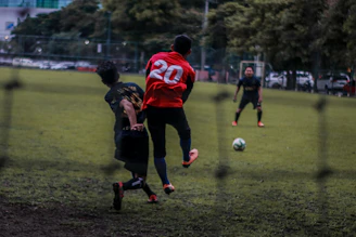 2 boys playing soccer on green grass field during daytime