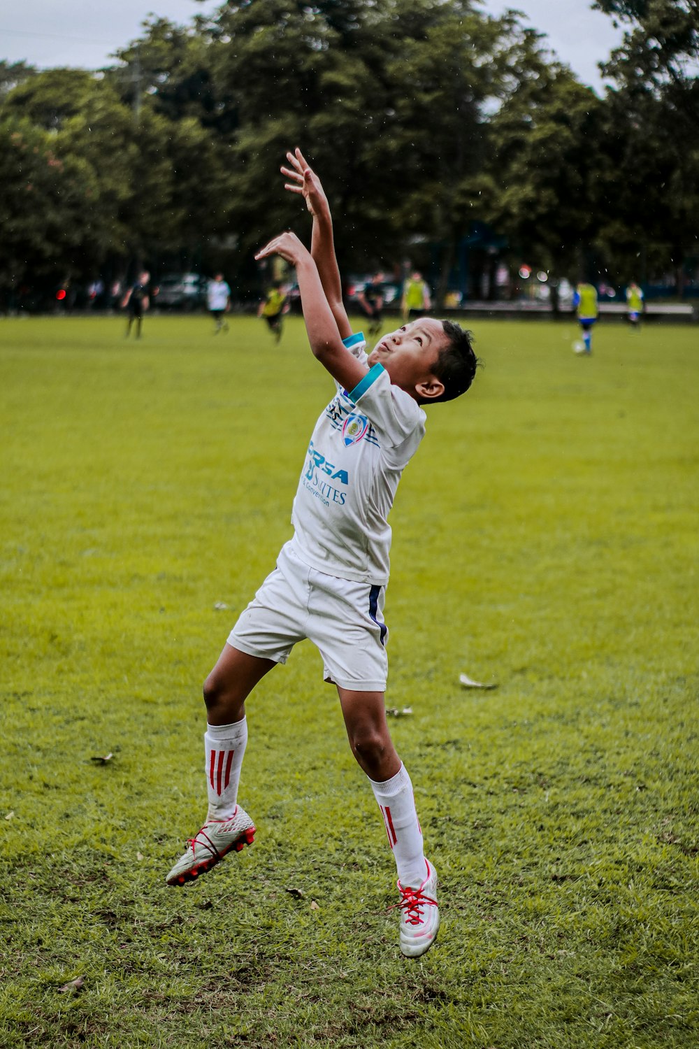 homme en maillot de football blanc frappant un ballon de football sur un terrain d’herbe verte pendant la journée