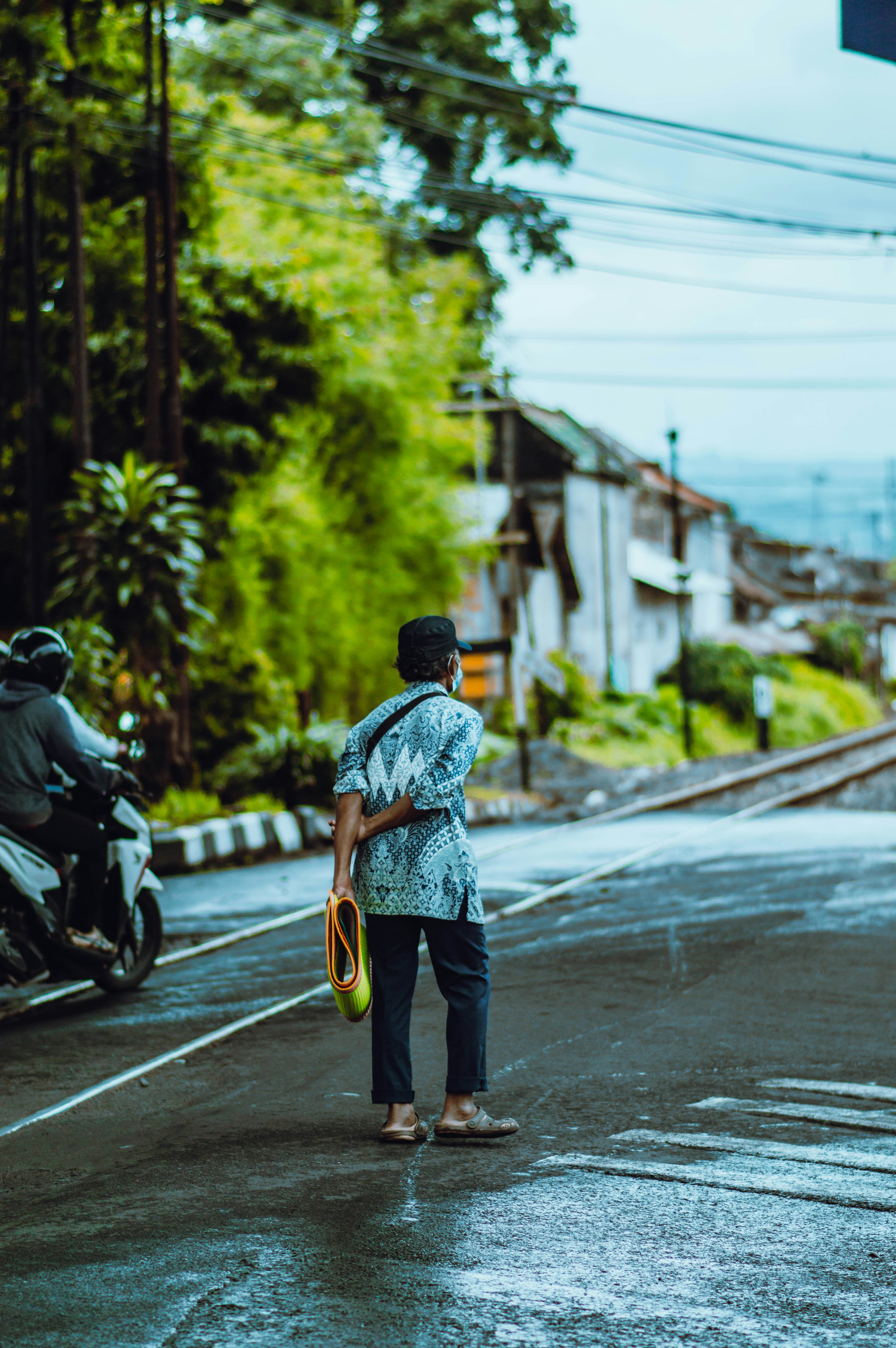Pria dengan kemeja kotak-kotak biru dan putih dan celana hitam berjalan di trotoar di siang hari
