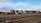 Stacks of colorful shipping containers are piled next to a set of railway tracks. The containers bear branding from various shipping companies, and the area appears to be part of a shipping yard or freight terminal. The sky is clear with some scattered clouds.