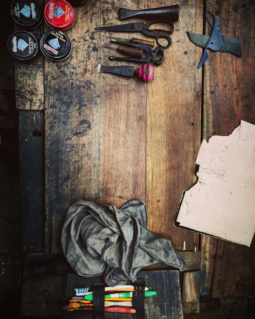 Close-up of a vintage industrial table scattered with colorful yarns, handmade greeting cards, and paintbrushes