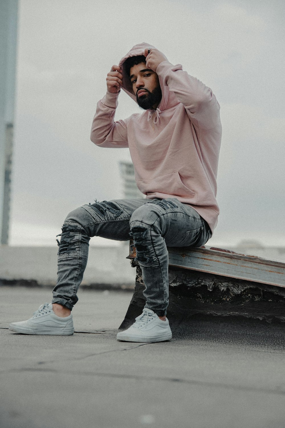 man in pink hoodie and blue denim jeans sitting on brown wooden bench during daytime