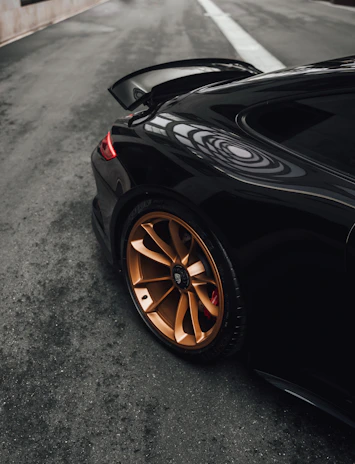 Side profile of a new black sports car with golden rims parked on a dark reflective surface.