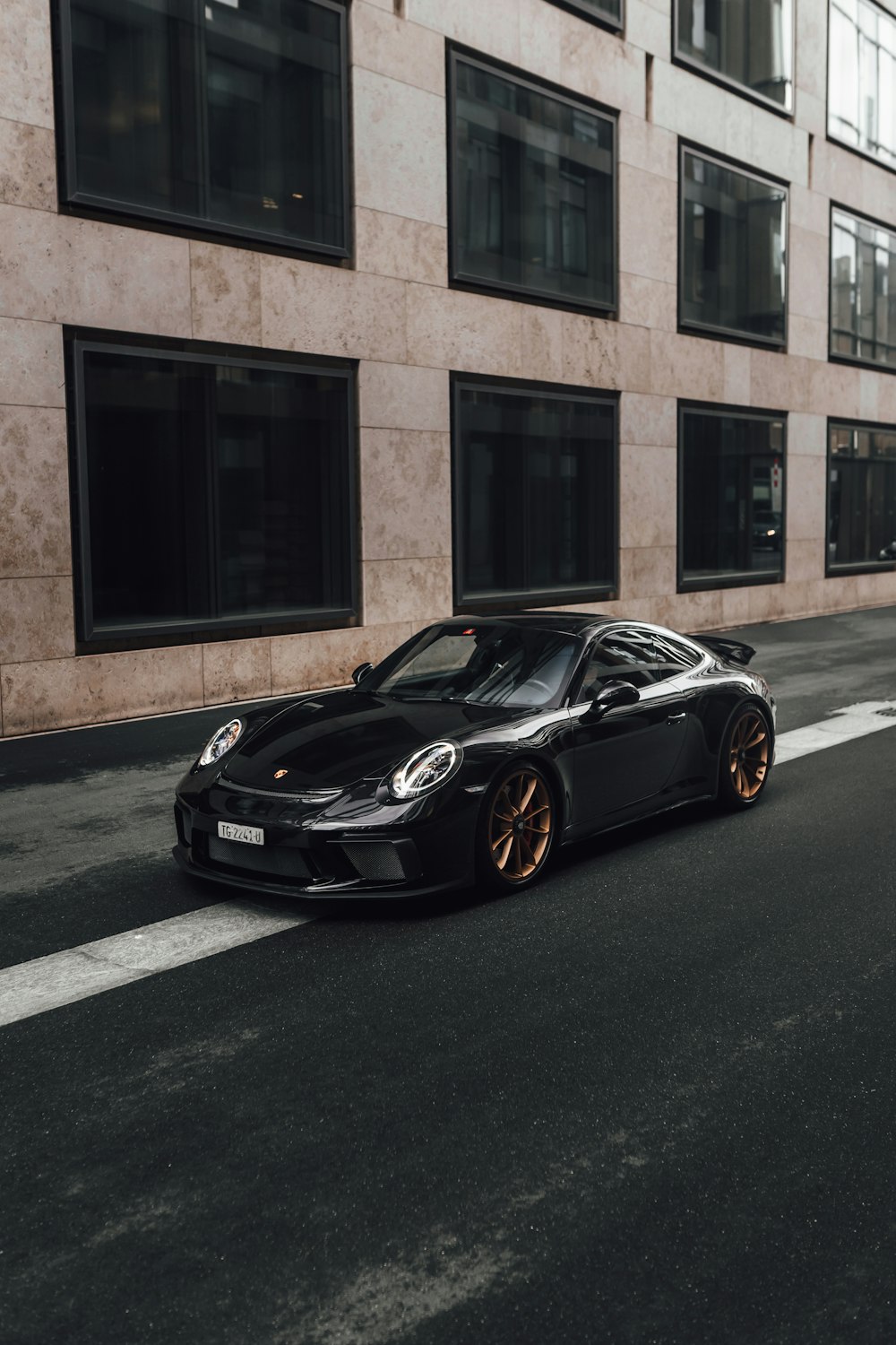 Porsche 911 negro estacionado cerca de un edificio de concreto marrón durante el día