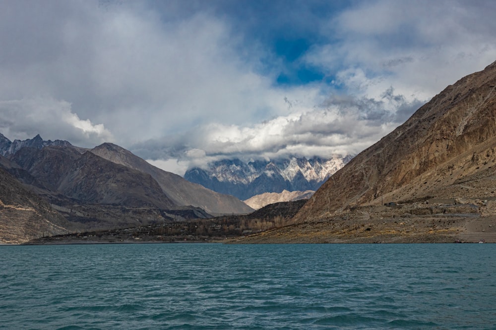 brown and green mountains beside body of water under white clouds and blue sky during daytime