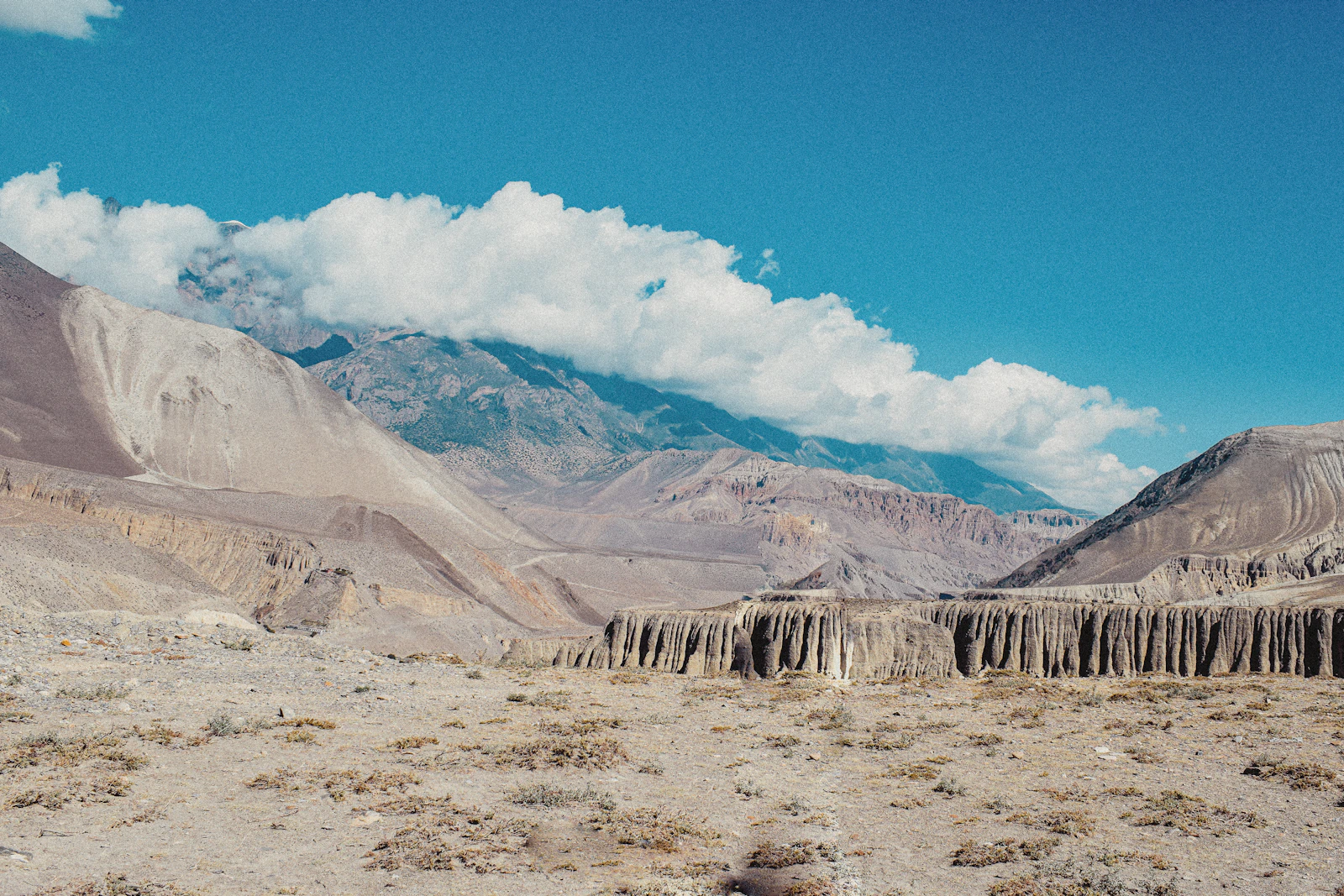A wide Mustang high-desert valley with chortens and a line of layered ochre hills