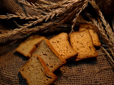 Slices of toasted bread are arranged on a textured burlap background, complemented by sprigs of wheat. The environment gives a rustic and homely feel.