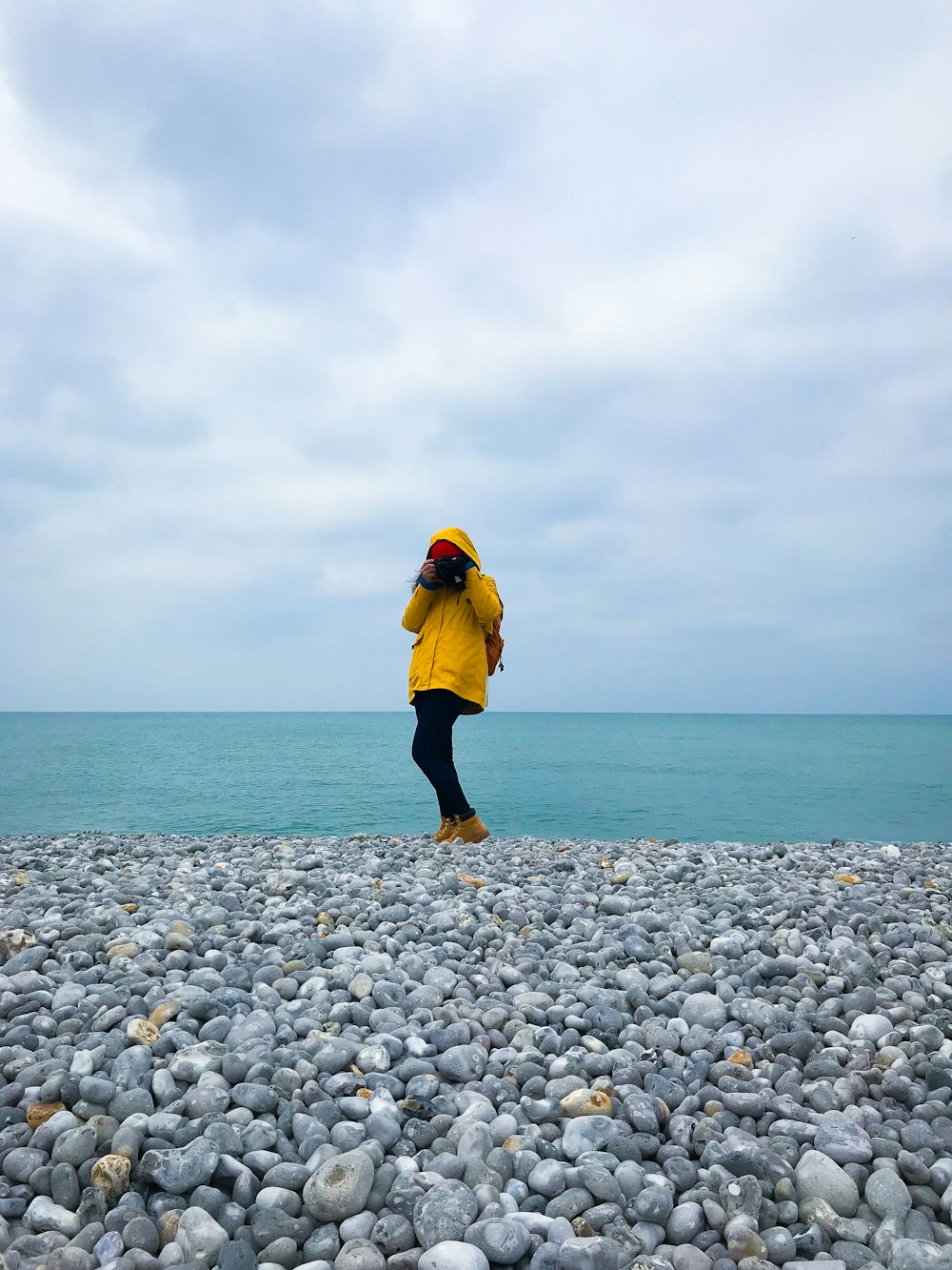 woman in yellow hoodie standing on gray and white pebbles near body of water during daytime