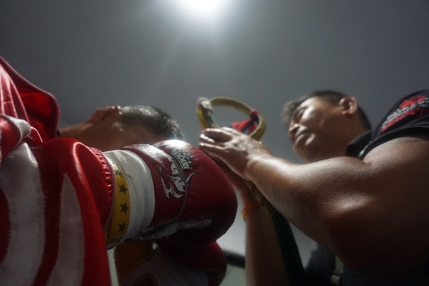 A close-up of a boxer lacing up balmant athletics gloves in a dimly lit gym.
