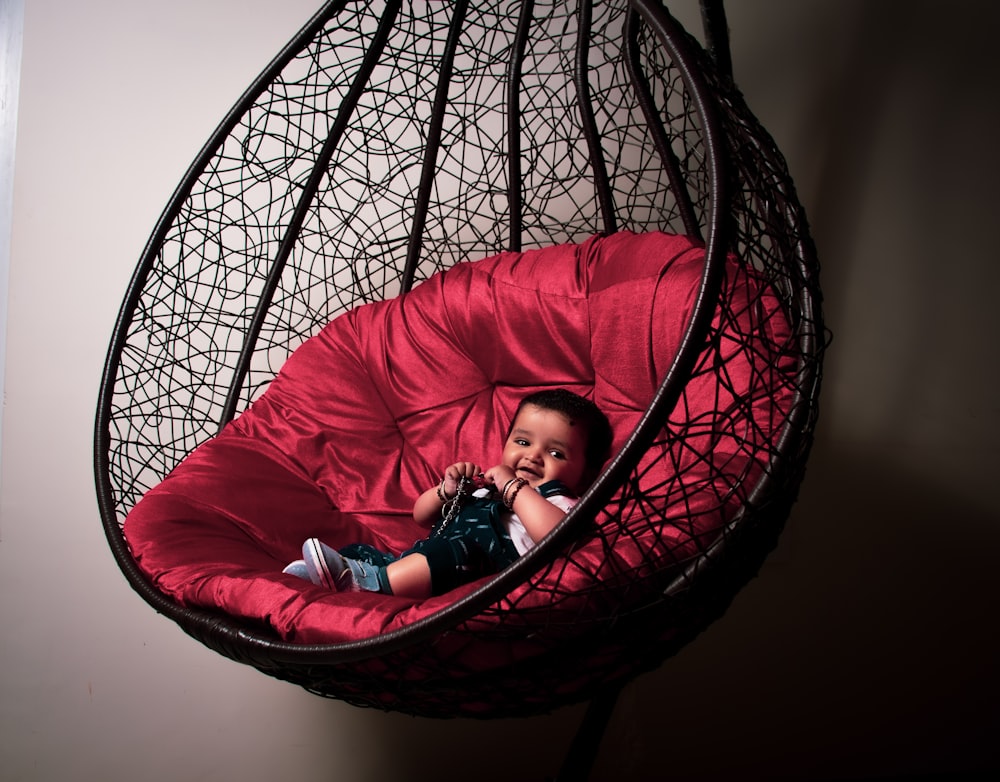 girl in pink jacket lying on red and black hammock