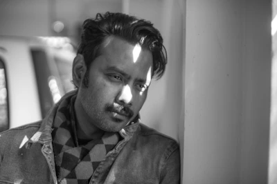 An editorial black and white photo of a man in a dramatic pose against a textured wall.