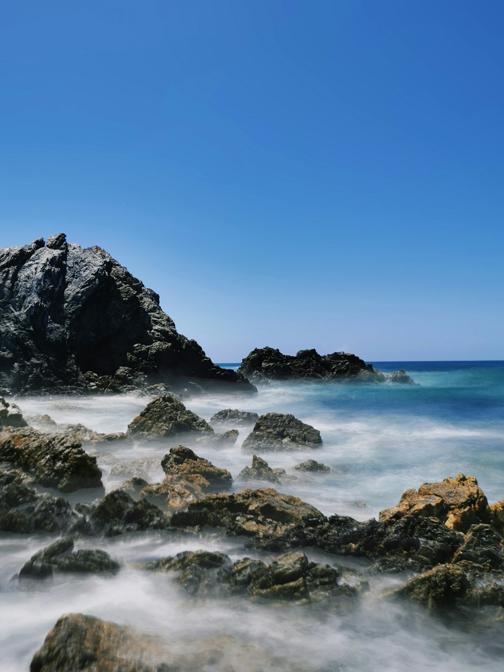 black rock formation on sea under blue sky during daytime