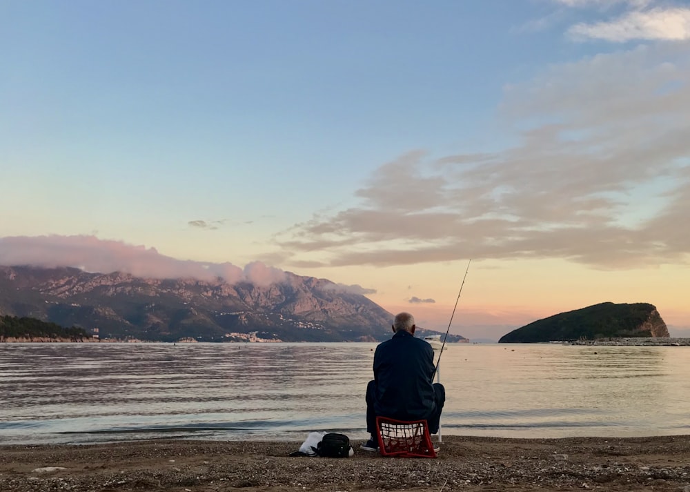 man in black jacket sitting on red and white fishing rod during daytime