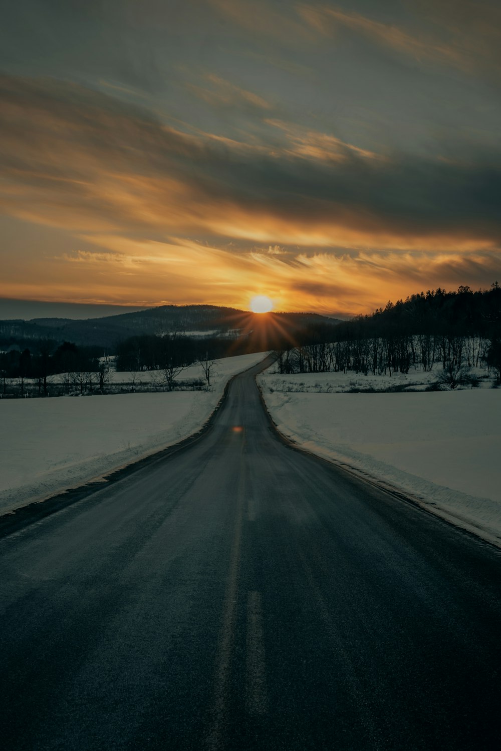 estrada de concreto cinza entre o solo coberto de neve durante o pôr do sol