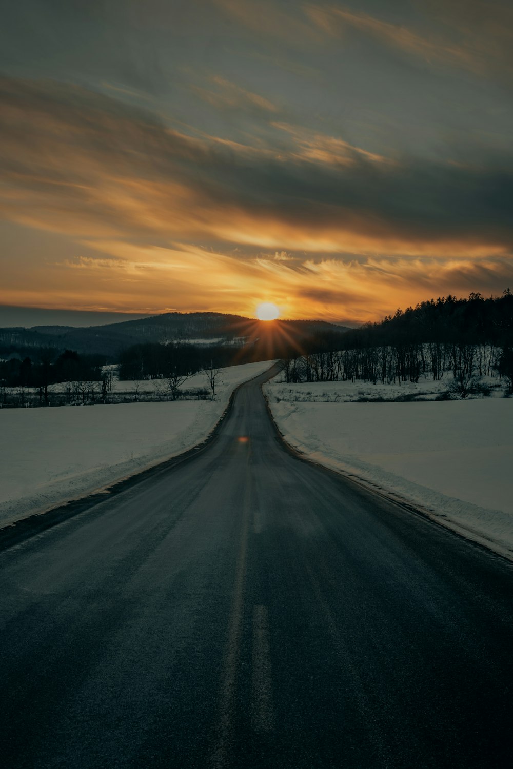strada di cemento grigio fra il terreno coperto di neve durante il tramonto