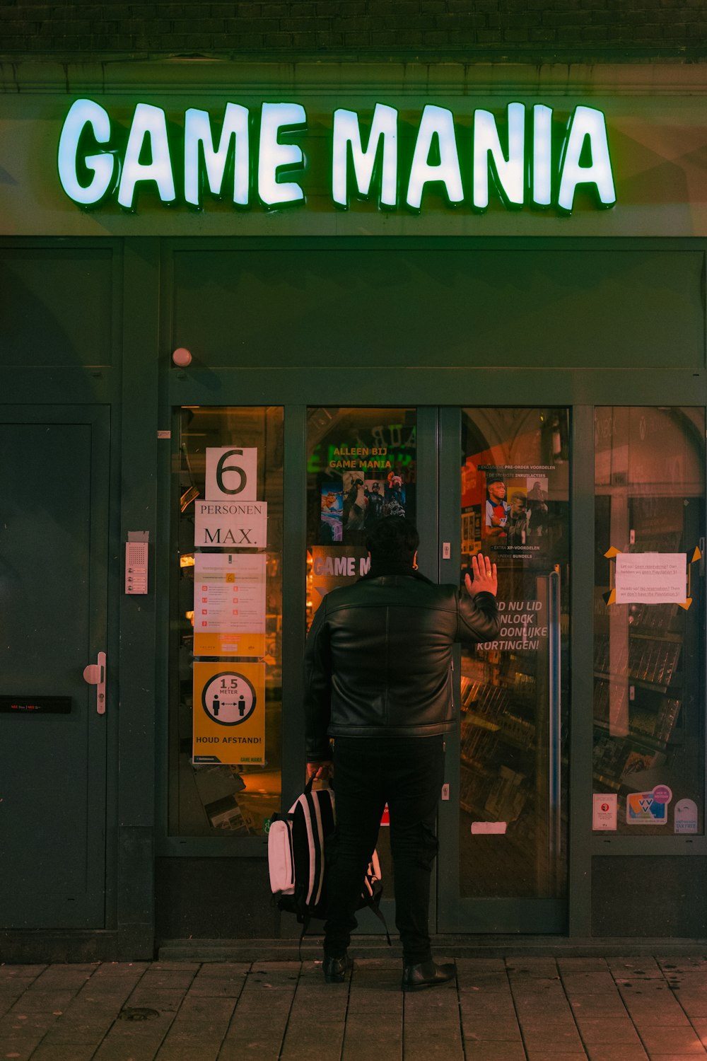 Hombre con chaqueta de cuero negro de pie cerca de la tienda verde y marrón