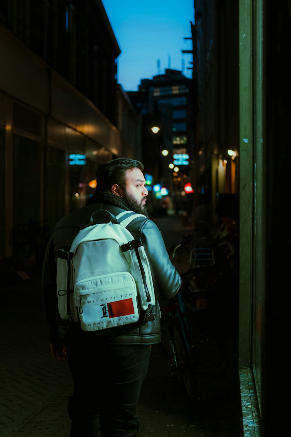 man in black and white backpack standing in front of store during night time