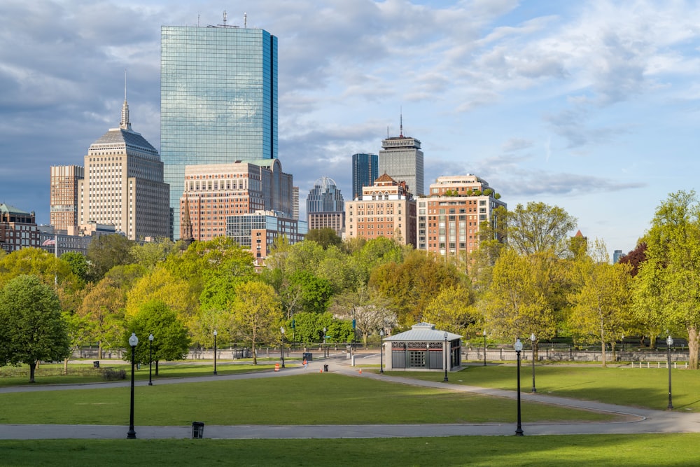 green grass field with trees and buildings in distance under white clouds and blue sky during