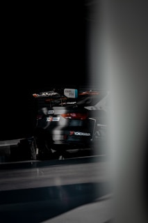 A sleek, dark-colored racing car with prominent sponsor logos such as Audi Sport, TCR Europe, and Yokohama. The car is set against a dimly lit background, giving it a dramatic appearance.