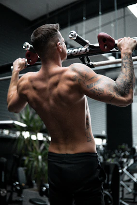 An athlete performing a controlled pull-up against a dark gym background with red glow accents highlighting their form.