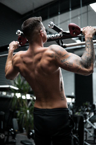 An athlete performing a powerful pull-up against a dark gym backdrop with red glow accents.