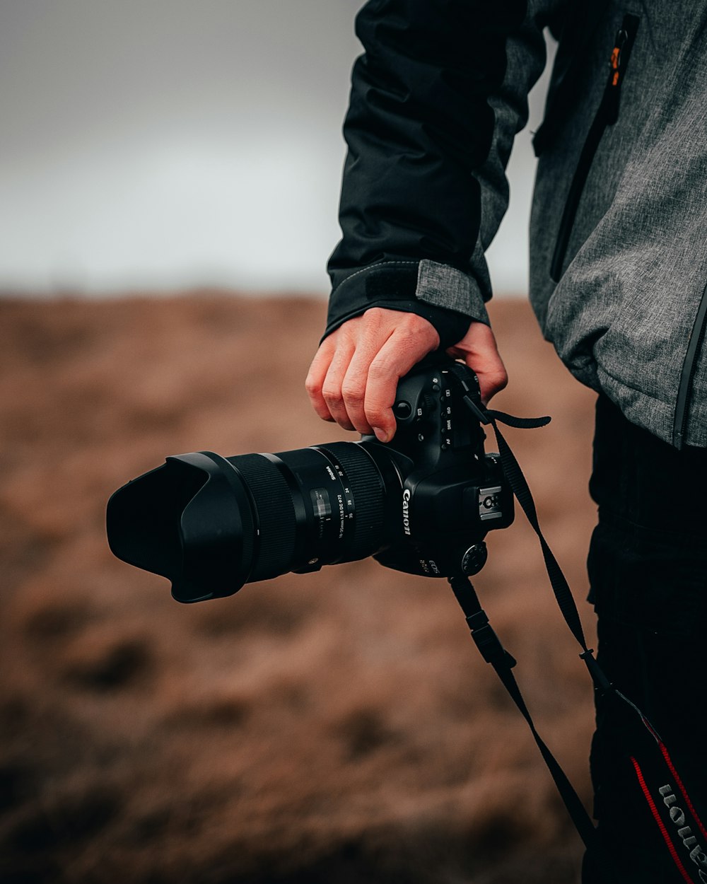 Person in grauer Jacke mit schwarzer DSLR-Kamera