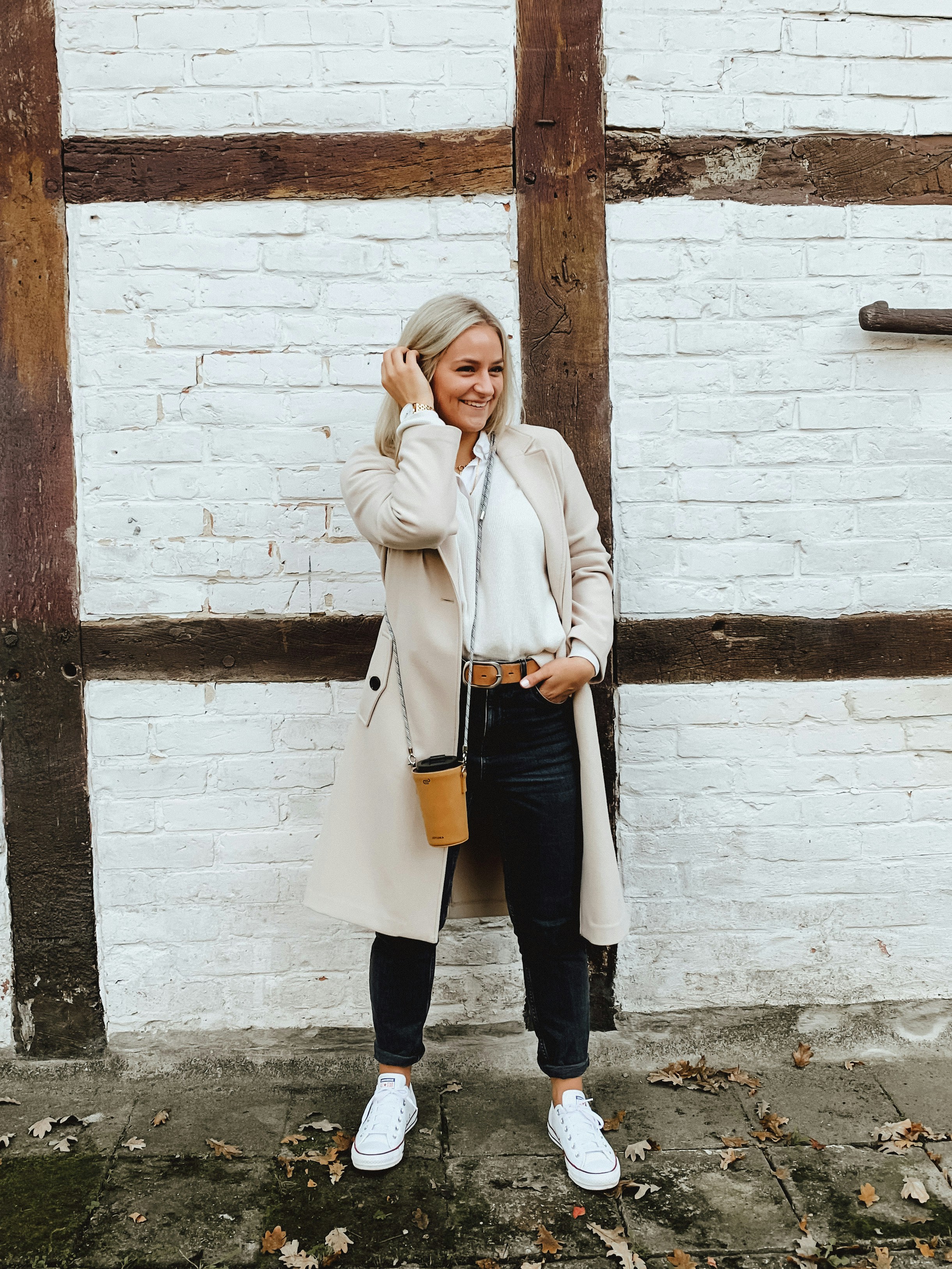 woman in white coat and black pants standing beside brown brick wall