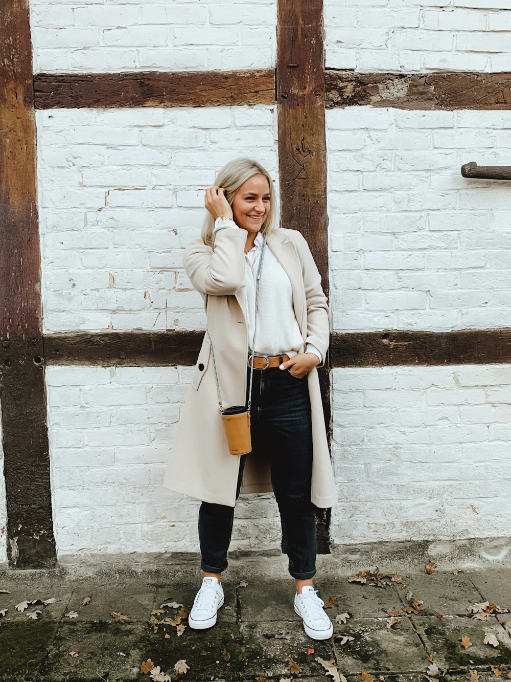 woman in white coat and black pants standing beside brown brick wall