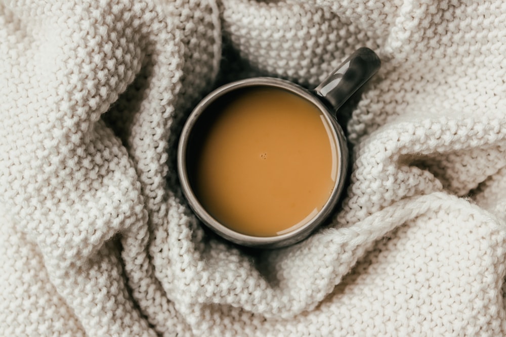 brown liquid in clear glass mug on white knit textile