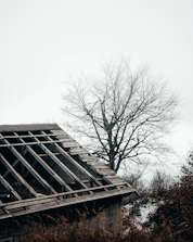 Image of a UK house roof with visible sagging and missing tiles under cloudy sky.