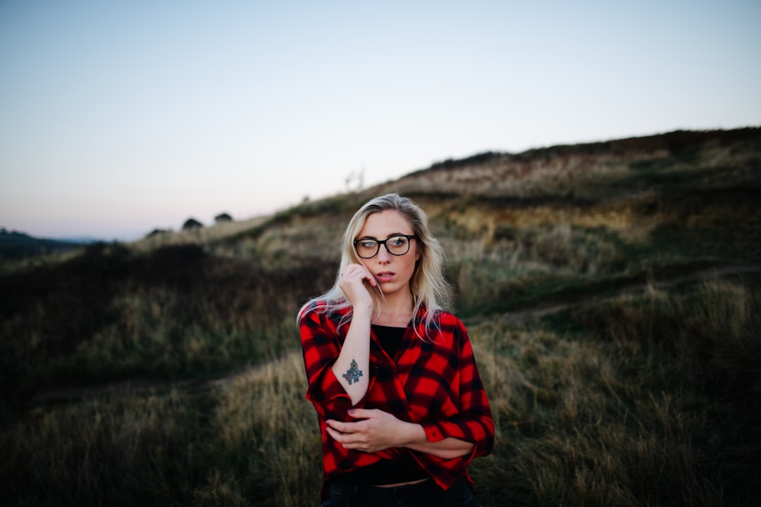 woman in red and black checkered long sleeve shirt wearing eyeglasses standing on green grass field
