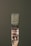 A paintbrush bristling with dark green paint stands vertically against a matching green background. The handle bears signs of wear, with paint splatters and the marking '25MM' visible. The bristles are coated with thick, wet paint.