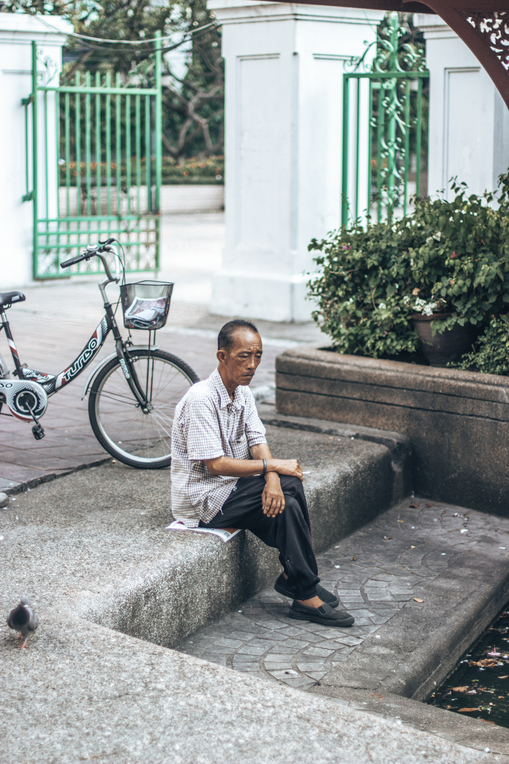 man in white button up shirt and black pants sitting on concrete bench beside bicycle during