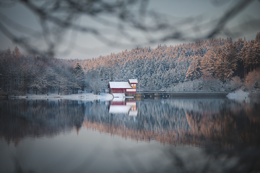 white and red house near lake surrounded by trees under white clouds during daytime