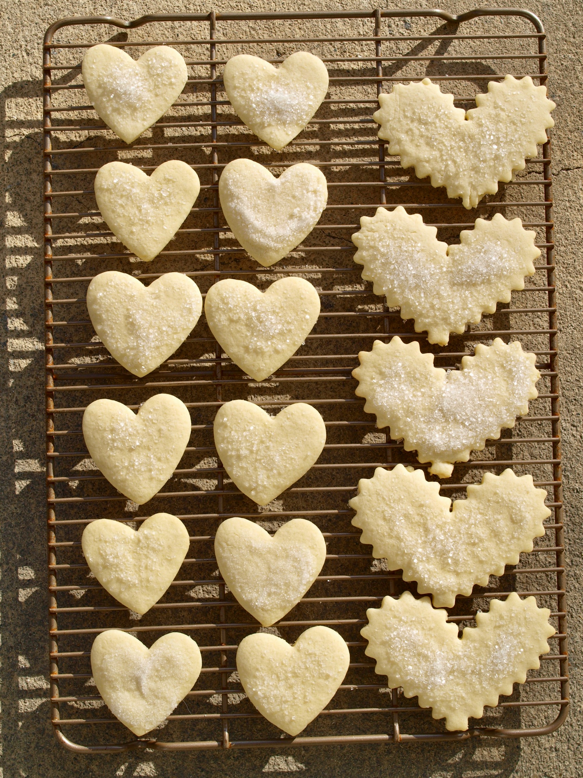 A homemade batch of German sugar cookies, rolled and cut into two different heart shapes, cools on a cookie rack.